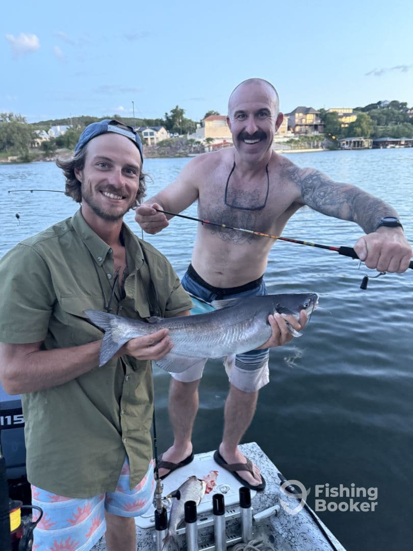 Two anglers proudly displaying a large catfish while fishing on a lake, showcasing a fun day on the water.