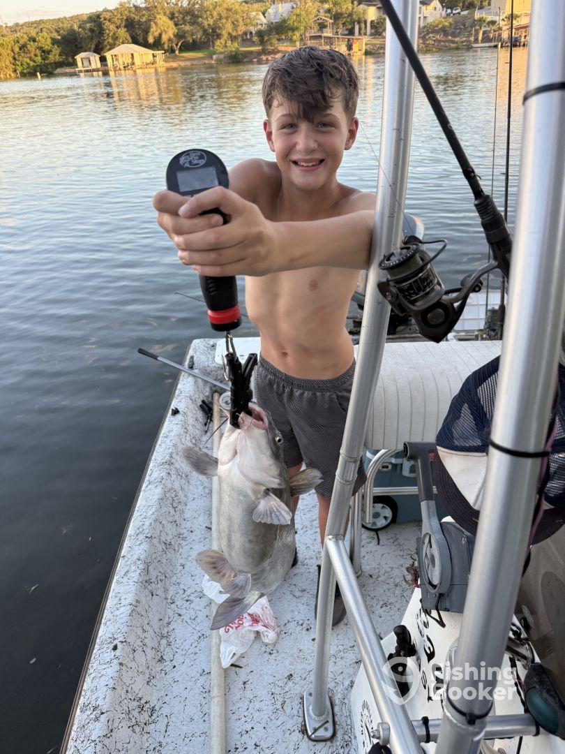 A young angler proudly displaying a large catfish while fishing from a boat on a serene lake.