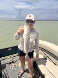 Angler proudly displaying a Speckled Trout while fishing from a boat in coastal waters.