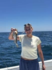 A young angler proudly displaying a caught fish while fishing on a boat in open waters.