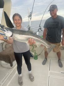 A young angler proudly displaying a large Salmon while fishing on a boat, showcasing a successful day on the water.