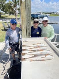 Three anglers proudly display their catch of Redfish on a cleaning table at a dockside location, showcasing a successful day of fishing.