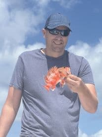 An angler proudly displaying a vibrant Red Snapper against a backdrop of clear blue skies, showcasing a successful fishing trip.
