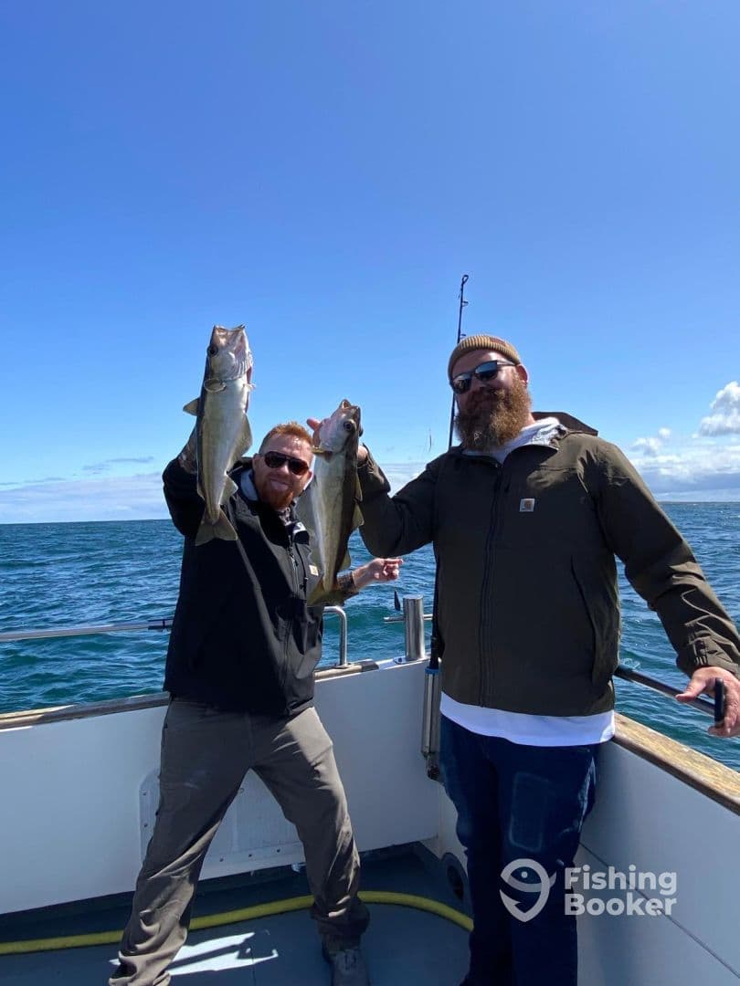 Two anglers proudly displaying their catch of Cod while fishing on a boat in open waters.