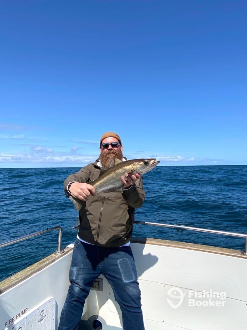 Angler proudly displaying a large fish on a boat in open waters, showcasing a successful fishing trip.