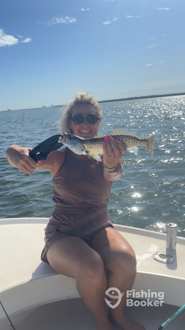 Angler proudly displaying a Speckled Trout while enjoying a sunny day on the water.