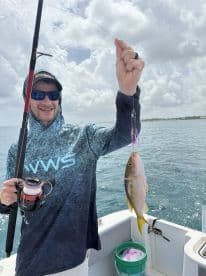A young angler reeling in a Yellowtail Snapper while fishing on a boat, showcasing an exciting moment on the water.