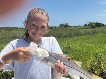 A young angler proudly displaying a Snook caught during a fishing trip in a lush coastal environment.