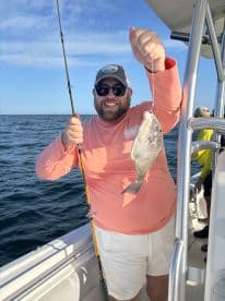 An angler proudly displaying a freshly caught Snapper while fishing on a boat in open waters.