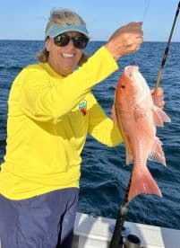 An excited angler proudly displaying a freshly caught Red Snapper while fishing on a boat in clear waters.