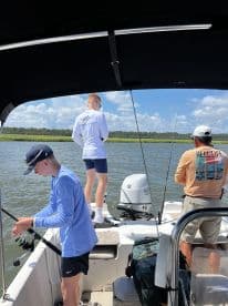 Two young anglers actively fishing from a small boat in a coastal waterway, showcasing a sunny day of fishing adventure.