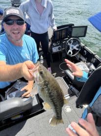 An enthusiastic angler proudly displaying a large Largemouth Bass while fishing on a boat, surrounded by family members.