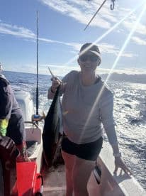 A proud angler displaying a large Tuna while fishing on a charter boat in clear blue waters.