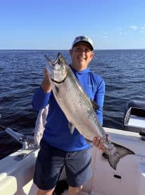 An angler proudly displaying a large Silver Salmon while fishing on a sunny day in open waters.
