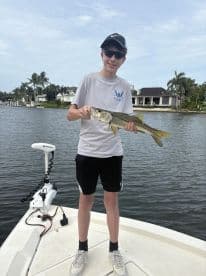 Young angler proudly holding a Snook while fishing from a boat in a scenic waterway.