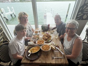 A family enjoying a meal at a waterfront restaurant, with a view of the water and dock in the background.