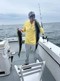 Angler proudly displaying two large Striped Bass while fishing on a charter boat in open waters.