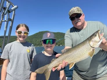 A young angler proudly displays a large Lake Trout while enjoying a sunny day on the water with family.