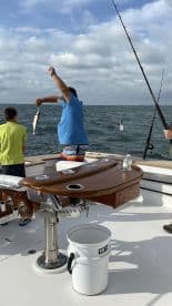 A young angler is reeling in a fish while another child watches on a fishing charter in open waters.