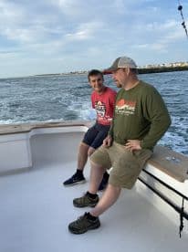 Two anglers enjoying a moment on the boat, with a scenic view of the coastline in the background.