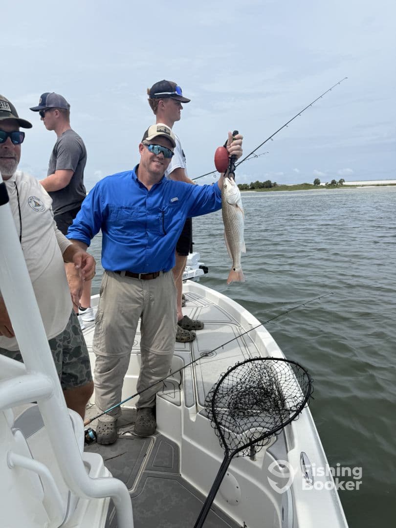 Angler proudly displaying a Redfish while fishing on a boat, with fellow anglers in the background enjoying a day on the water.