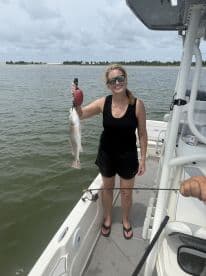 An angler proudly displaying a freshly caught Redfish while standing on a boat, showcasing a successful day of fishing in coastal waters.