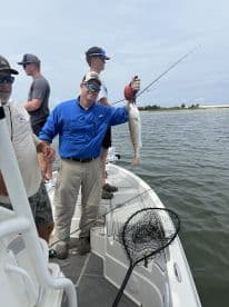 Angler proudly displaying a Redfish while fishing on a boat, with fellow anglers in the background enjoying a day on the water.