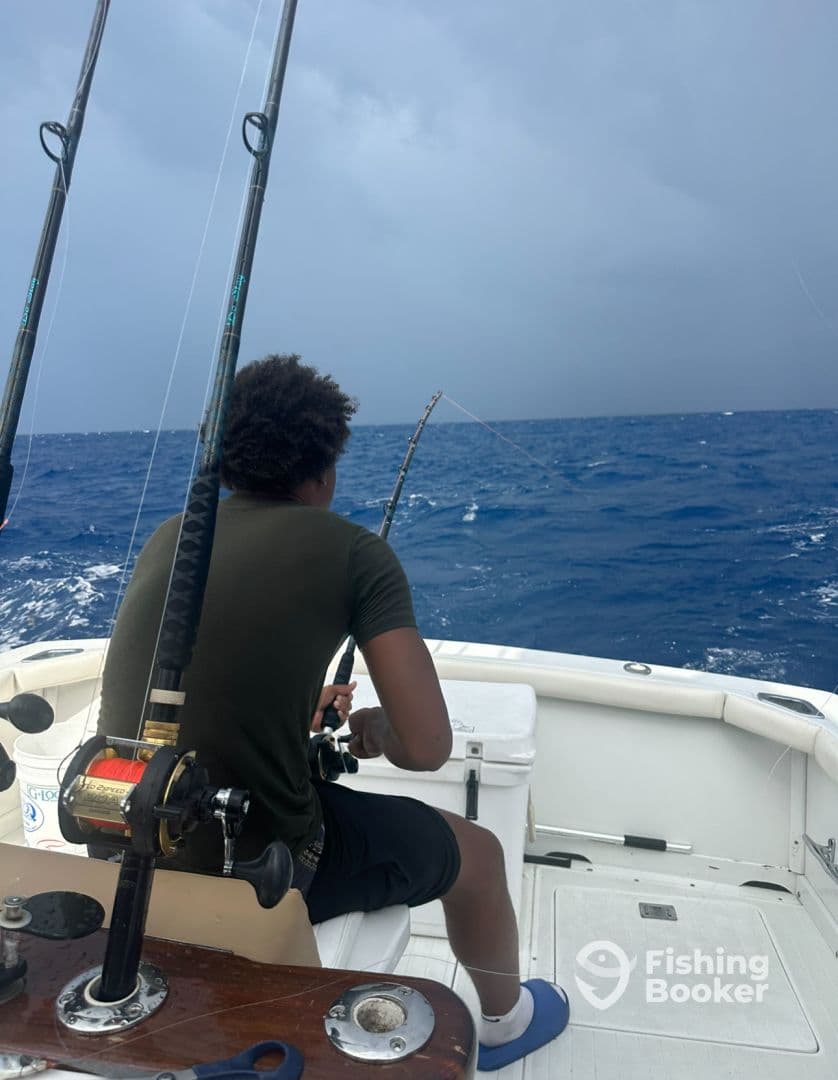 A young angler focused on reeling in a catch while fishing offshore, surrounded by open water and a cloudy sky.