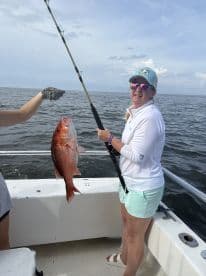 Angler proudly displaying a large Red Snapper while fishing on a boat, showcasing a successful day on the water.