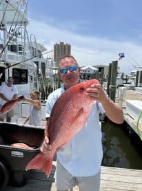 An angler proudly displaying a large Red Snapper at the marina, showcasing a successful fishing trip.