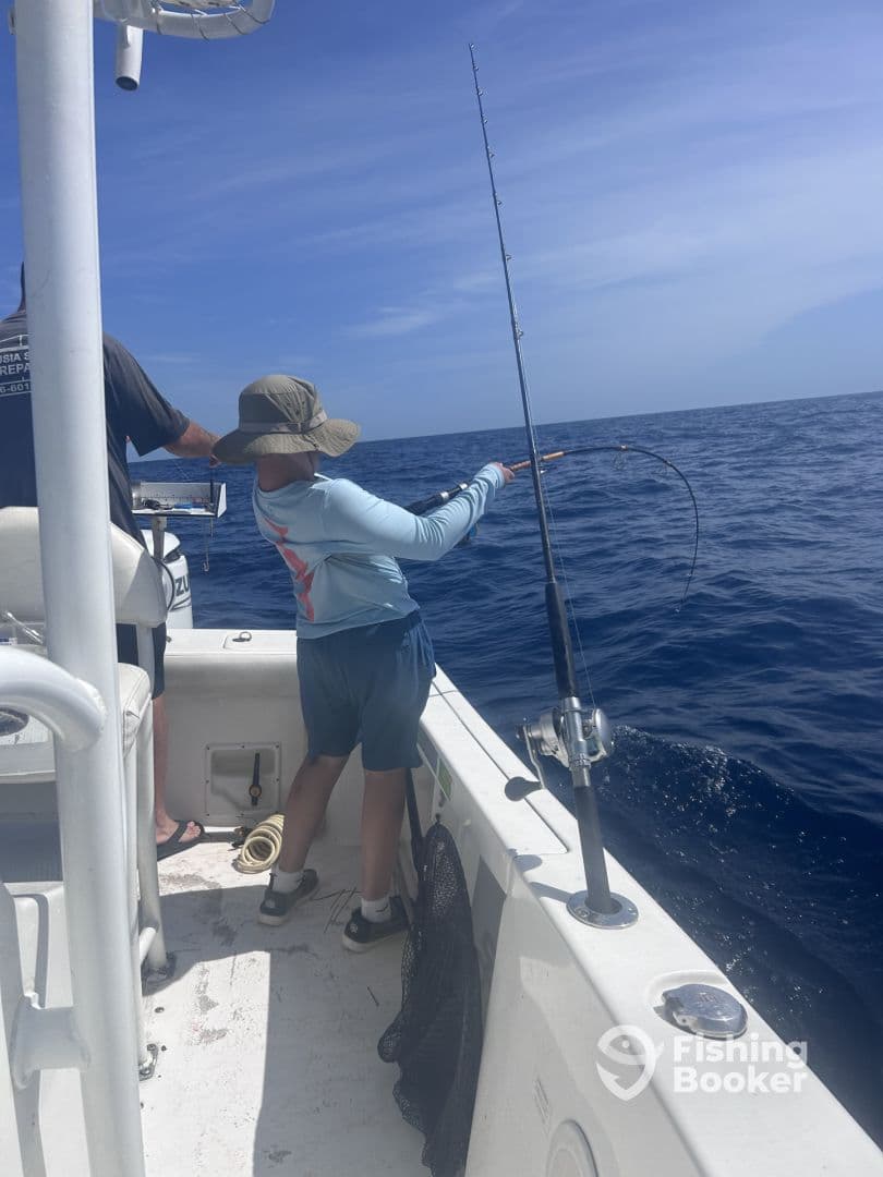 A young angler actively reeling in a fish while fishing on a boat in open water, showcasing the excitement of deep-sea fishing.