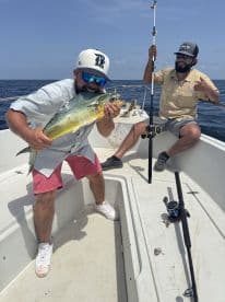 Two anglers aboard a boat, with one proudly displaying a large Mahi Mahi caught during a deep-sea fishing trip.