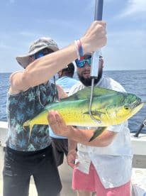 Two anglers proudly displaying a vibrant Mahi Mahi while fishing offshore, showcasing a successful day on the water.
