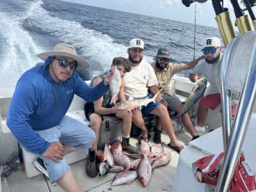 A group of anglers on a boat displaying their catch, including several Snapper and a Mahi Mahi, showcasing a successful day of fishing in open waters.