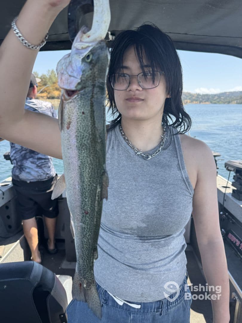 A young angler proudly displaying a Rainbow Trout while fishing on a boat, showcasing a beautiful day on the water.