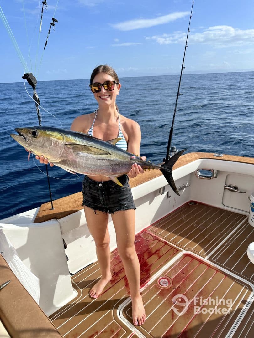 An angler proudly displaying a large Yellowfin Tuna on a fishing boat, showcasing a successful offshore fishing trip.