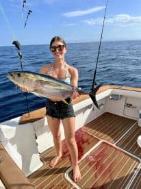 An angler proudly displaying a large Yellowfin Tuna on a fishing boat, showcasing a successful offshore fishing trip.