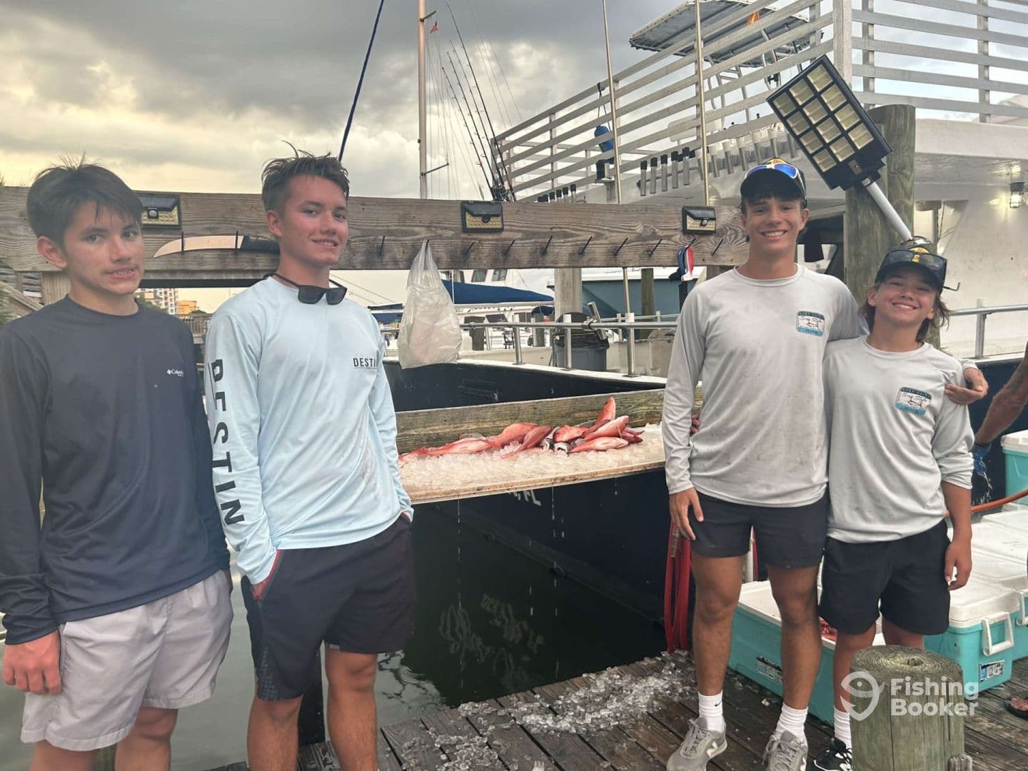 A group of young anglers posing by a catch board displaying several fish after a successful fishing trip at the dock.