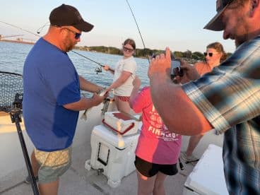 A group of young anglers enjoying a fishing trip, with one child holding a fish while others capture the moment on their phones.