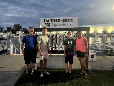 A family poses in front of a catch board displaying several fish after a successful fishing trip with In The Box Fishing Charters.