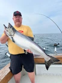 An angler proudly displaying a large Salmon while fishing on a boat, showcasing a successful day on the water.