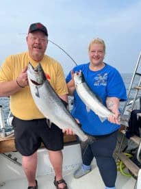 Two anglers proudly displaying their catch of Salmon while fishing on a boat.