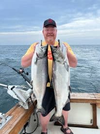 Angler proudly displaying two large Chinook Salmon while fishing on a charter boat in open waters.