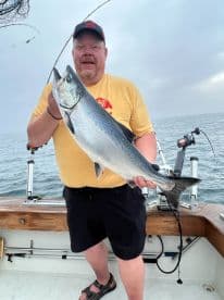 An angler proudly displaying a large Salmon while fishing on a boat, showcasing a successful day on the water.