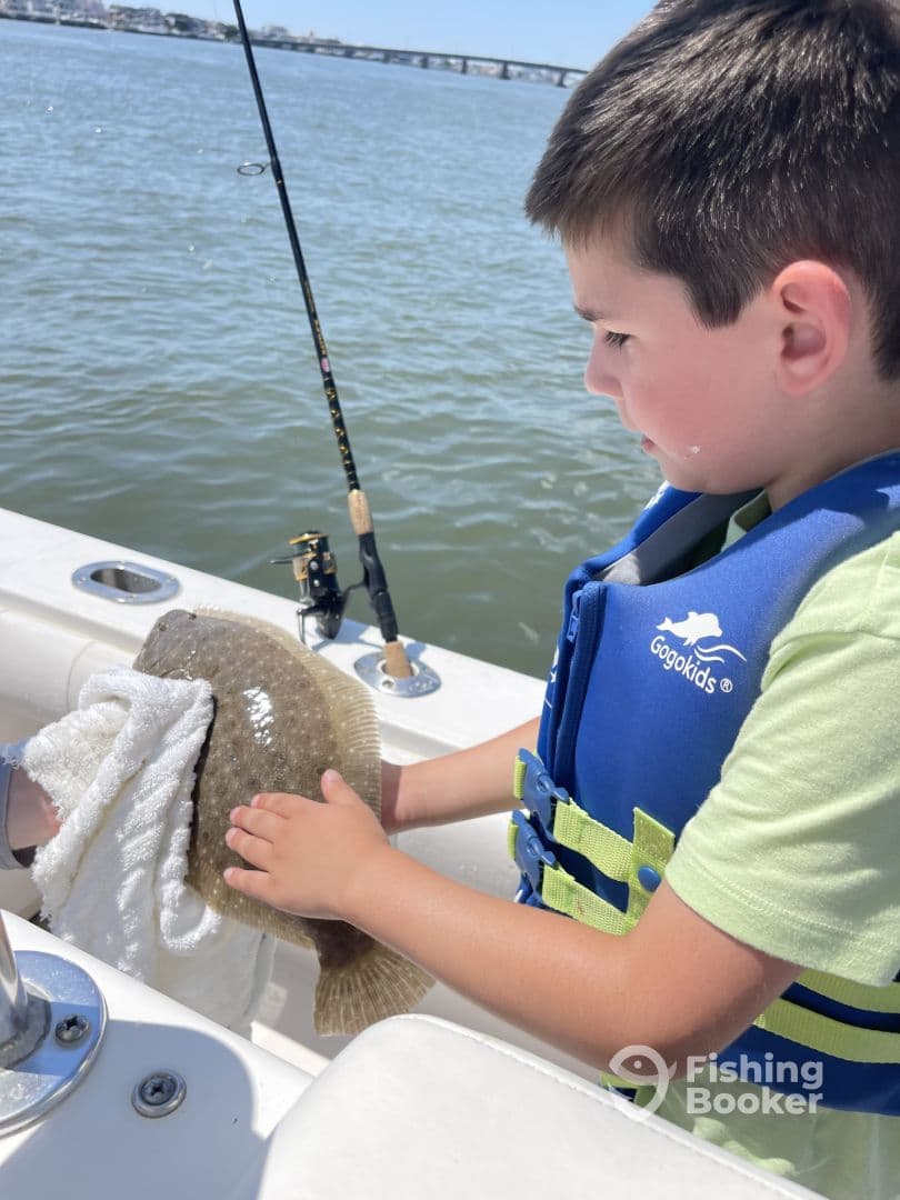 A young angler holding a Flounder while fishing from a boat, showcasing a proud moment on a sunny day.