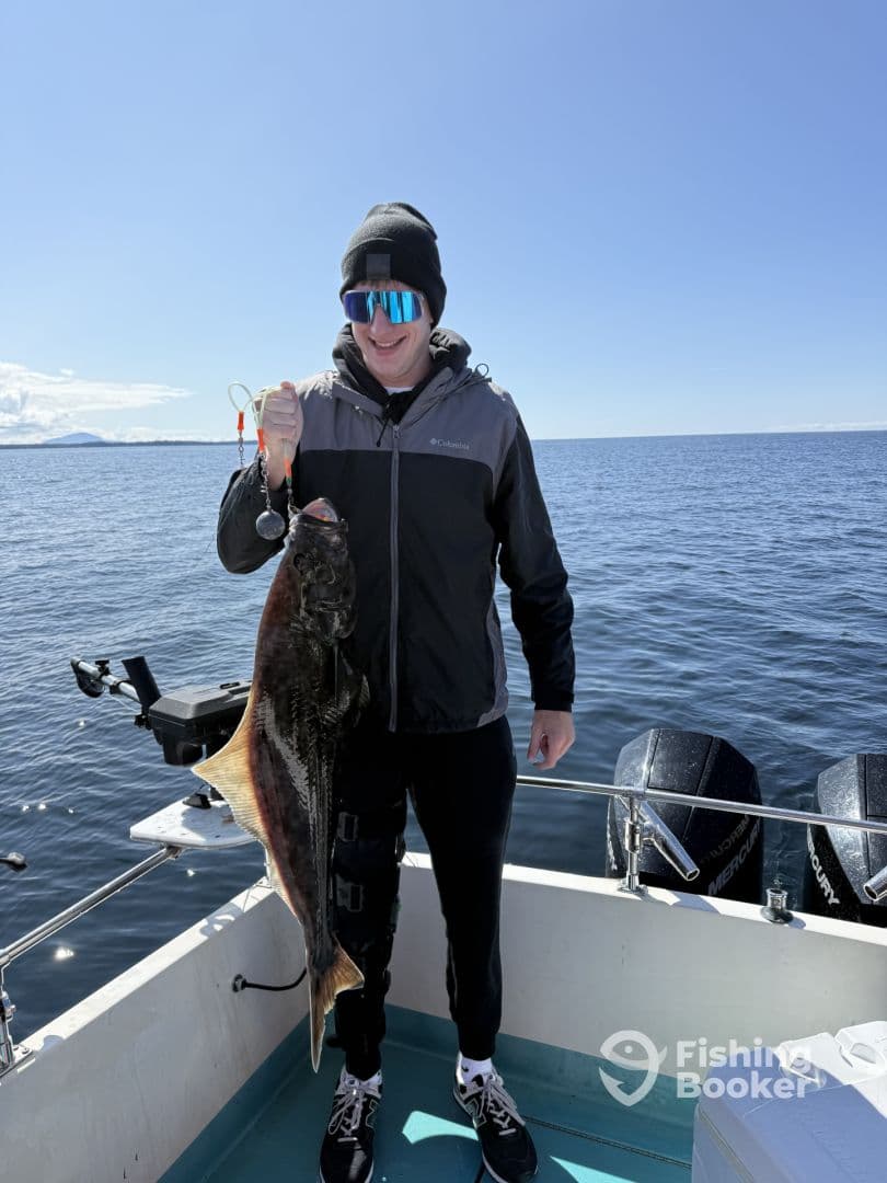Angler proudly displaying a large Halibut while fishing on a boat in open waters.