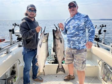 Two anglers proudly displaying their catch of Salmon while fishing on a boat in open waters.