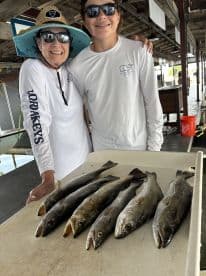 A proud family moment with a young angler and an adult displaying a catch of Speckled Trout on a dock after a successful fishing trip.