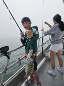 A young angler is reeling in a sizable fish while fishing on a boat, showcasing the excitement of a foggy day on the water.