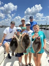 A family group proudly displaying their catch of Flounder aboard a boat, enjoying a sunny day on the water.